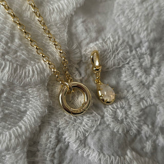 14k Gold openable clasp charm holder necklace featuring a unique dog clasp pendant necklace and a teardrop Genuine Moonstone charm with a clear faceted stone, displayed on a textured white fabric background