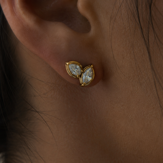 A close-up of a person's ear wearing a pair of gold butterfly stud earrings with clear marquise-cut gemstones.