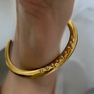 Gold bracelet with small diamonds on a wrist against a neutral background