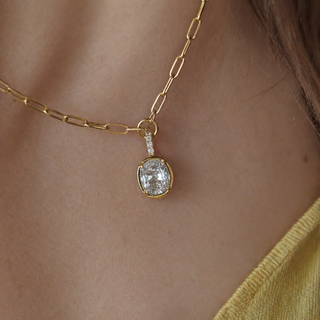 Gold necklace with a bezel set Oval moissanite pendant on a person's neck on a fine dainty paperclip chain