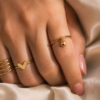 Close-up of a hand wearing gold heart-shaped rings on a beige fabric background