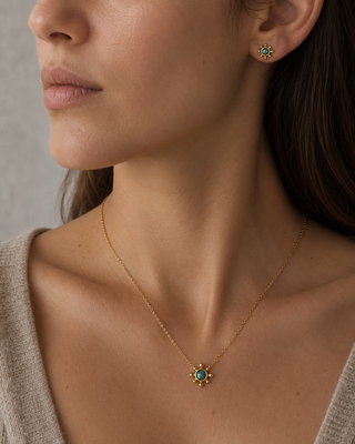 Close-up of a woman wearing a Blue grren fire opal gem gold necklace and earrings with green gemstones against a neutral background.