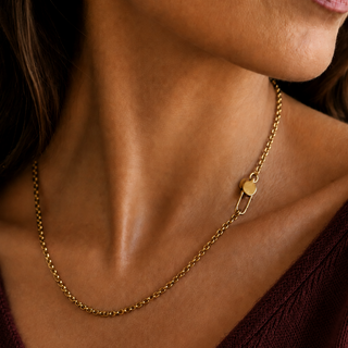 A close-up of a model wearing a delicate gold chain necklace with a small curved U pin Shaped openable charm holder clasp, paired with a dark burgundy V-neck top.