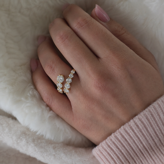 A close-up of a hand wearing a delicate gold ring set with clear round gemstones, resting on a soft white faux fur surface.