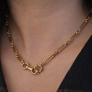 Gold chain necklace with a dog clasp charm holder carabiner worn by a person with a blurred background