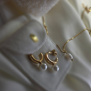 Gold and pearl earrings on a white textured surface