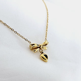 3 dimensional 18k gold daintybow detailed pendant with a dangle drop heart charm attached to it. 18k gold on stainless steel makes it tarnishfree and hypoallergenic.