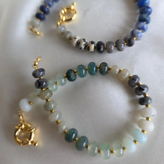 Two beaded bracelets with gold accents on a white fabric background